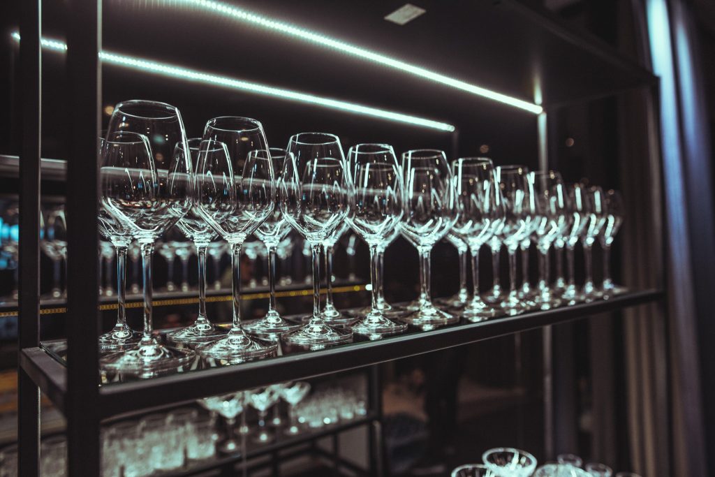 © Sergiu Andrés Row of tall wine glasses on a backlit bar display surface.