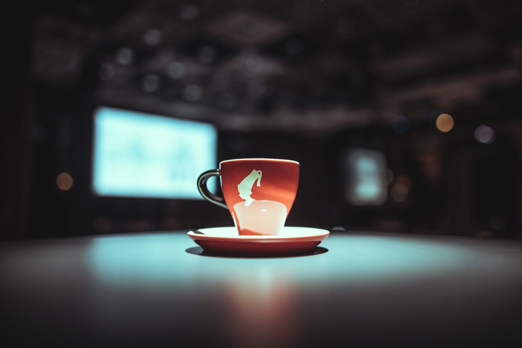 © Sergiu Andrés Red mug with a white graphic on a saucer, on a lit table with a dark, blurred background.