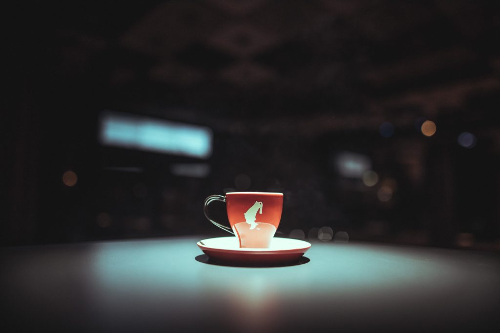 © Sergiu Andrés Red teacup with a white emblem on a matching saucer sits on a turquoise table, with blurred night lights in the background.