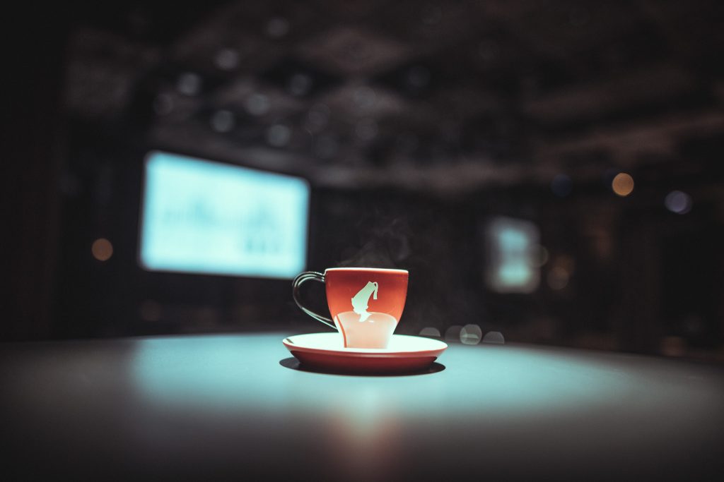 © Sergiu Andrés Red coffee cup on a matching saucer with steam rising, set on a dark table and a blurred bokeh background