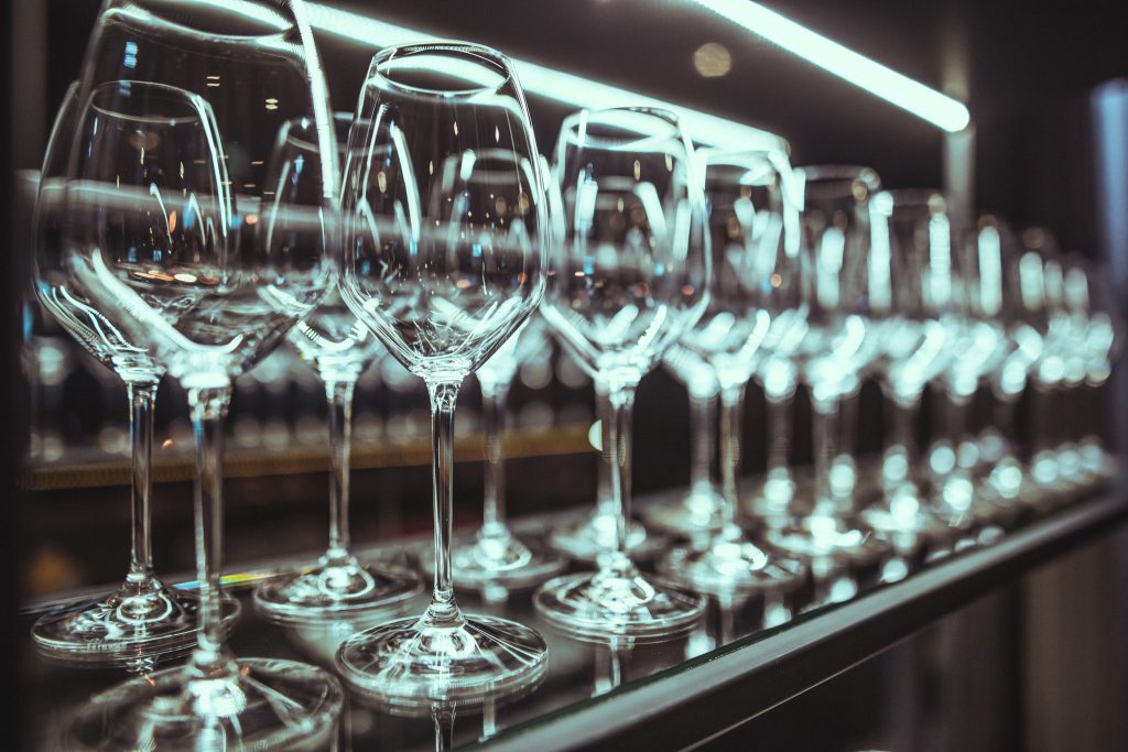 © Sergiu Andrés Row of wine glasses lined up on a mirrored bar surface with blue-tinted lighting and reflections.