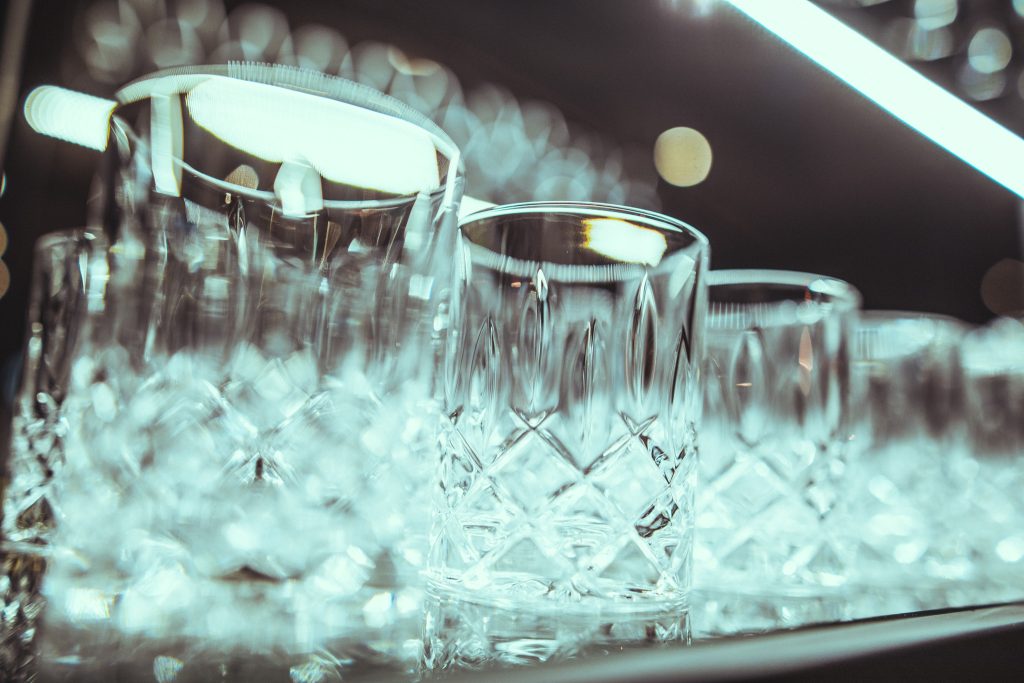 © Sergiu Andrés Row of crystal glasses with ice, reflections on the surface, soft bokeh lights in the background.