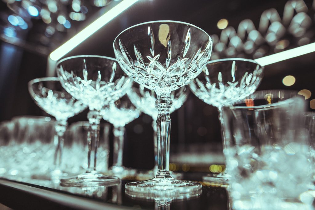 © Sergiu Andrés Close-up of a crystal champagne coupe on a bar, with blurred blue bokeh lights in the background.